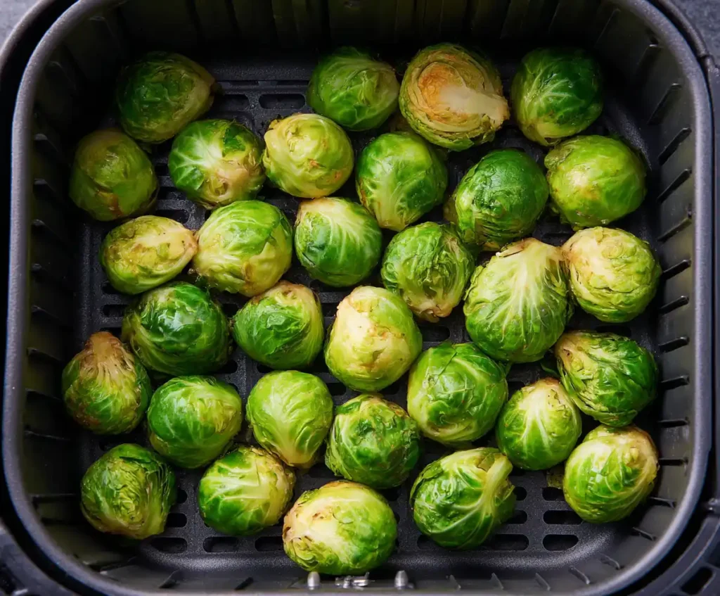 Brussels sprouts arranged in a single layer inside an air fryer basket, ready to cook