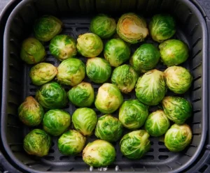Brussels sprouts arranged in a single layer inside an air fryer basket, ready to cook