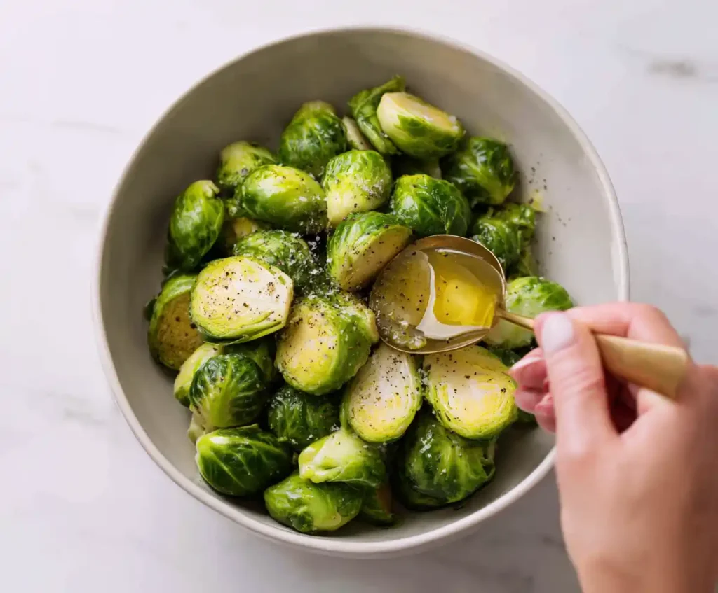 Brussels sprouts seasoned with olive oil, salt, and pepper in mixing bowl