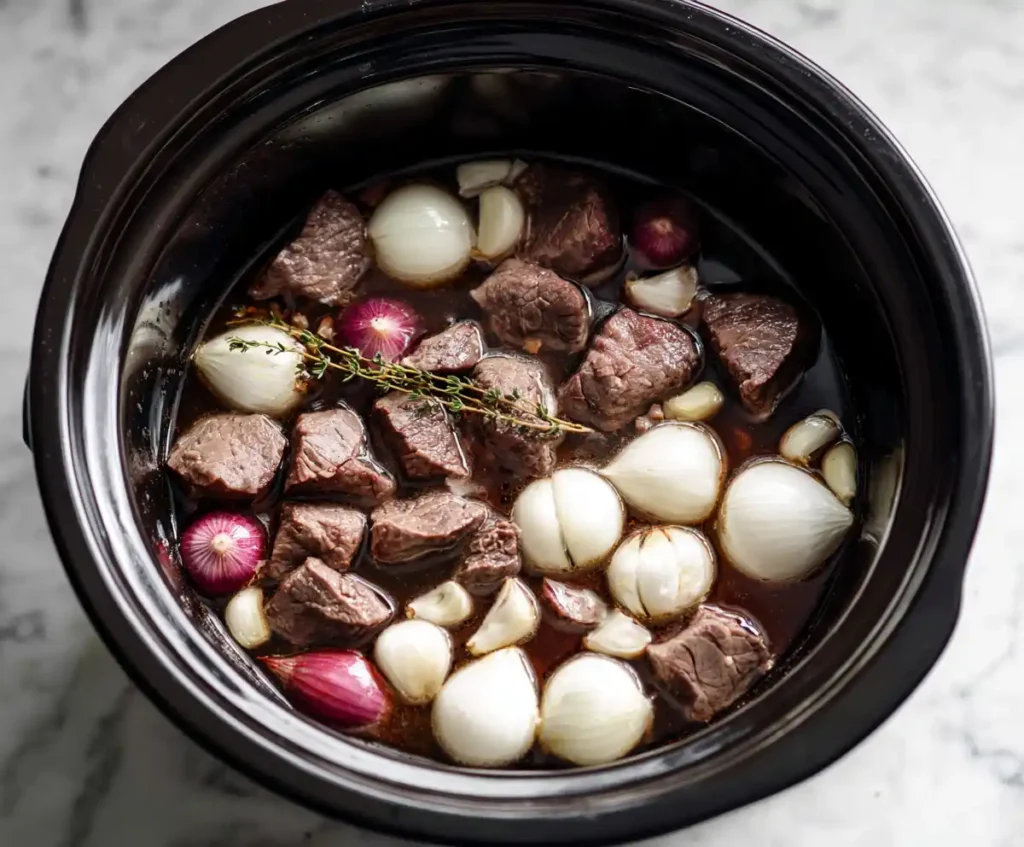 Beef broth with onions and garlic in slow cooker for French dip