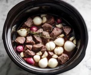 Beef broth with onions and garlic in slow cooker for French dip
