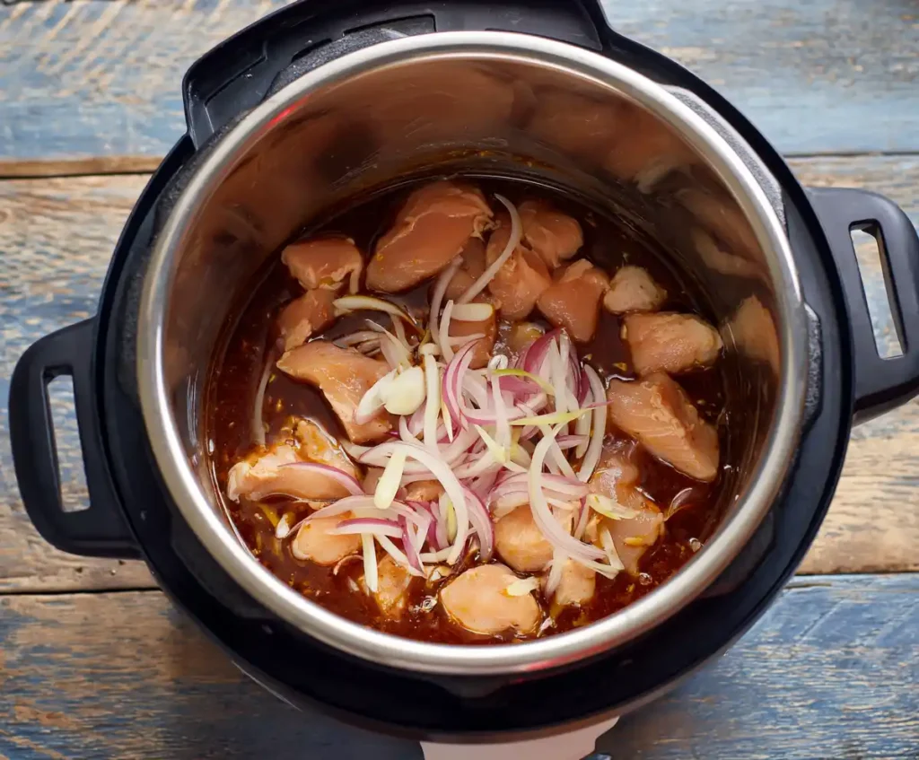 Raw chicken, onion, garlic with enchilada sauce in pressure cooker for chicken enchiladas