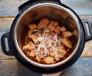 Raw chicken, onion, garlic with enchilada sauce in pressure cooker for chicken enchiladas