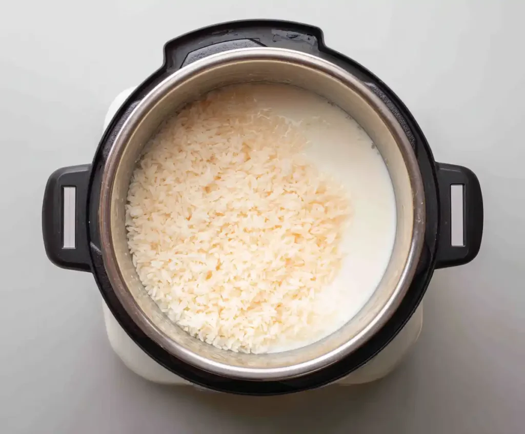 Rice, milk, and sugar in pressure cooker for rice pudding with raisins