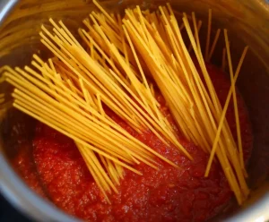 Uncooked spaghetti layered over sauce in Instant Pot before cooking